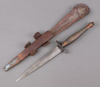 A Fairbairn-Sykes style second pattern commando fighting knife, the blade 17cm, unmarked to cross guard or Ricasso, complete with leather scabbard, (there is blacking to 1cm of the Ricasso which could infer an SOE sterile knife) 