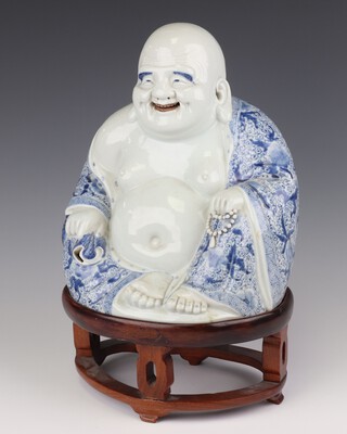 An early 20th Century ceramic figure of  seated Hotei with visible teeth 27cm on a wood stand