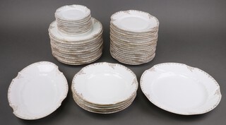 An early 20th Century Limoges dinner service with gilt floral rims comprising 10 small plates, 18 side plates, 12 dinner plates (4 chipped), serving dish (chipped), 5 soup bowls (3 chipped) and a circular serving plate 
