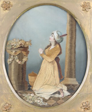 19th Century silk work embroidery of a lady praying before a column with painted face and hands, oval, 31cm x 26cm, contained in a gilt frame 