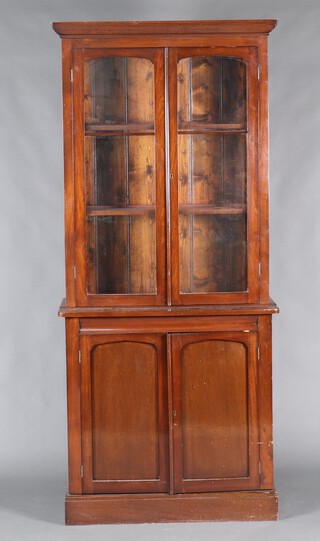 A Victorian mahogany bookcase on cabinet with moulded cornice, the shelved upper section enclosed by a glazed panelled door, the base enclosed by a pair of panelled doors, raised on a platform base 226cm h x 99cm w x 43cm d 