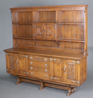 A carved oak dresser with moulded cornice to the raised back, fitted 2 shelves and cupboard enclosed by panelled doors, the base 4 long drawers flanked by cupboards 176cm h x 186cm w x 42cm d 