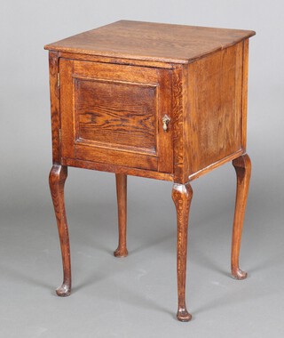 An Edwardian oak bedside cabinet enclosed by a panelled door, raised on cabriole supports 77cm h x 47cm w x 44cm d 