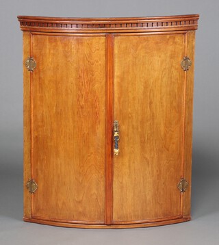 A Georgian mahogany bow front hanging corner cabinet with moulded and dentil cornice, fitted shelves enclosed by panelled doors 97cm h x 81cm w x 57cm d 