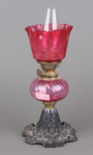 A Victorian cranberry glass and iron oil lamp with cranberry glass shade and reservoir, raised on a circular cast iron base 33cm x 13cm 