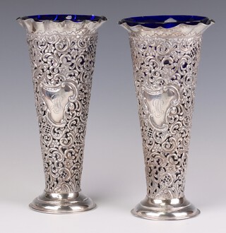 A pair of Victorian repousse pierced silver spill vases decorated with flowers and scrolls, engraved monogram Chester 1898, 22.5cm, with later blue glass liners, 1004 grams gross including the weighted bases 