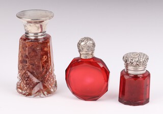 An Edwardian silver mounted ruby glass faceted scent bottle 4cm, a circular flattened ditto 5.5cm and a clear glass ditto 7cm 