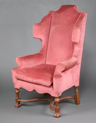 A Queen Anne style winged armchair upholstered in rose pink material, raised on carved scroll supports with X framed stretcher 132cm h x 80cm w x 60cm d (seat 31cm x 33cm)