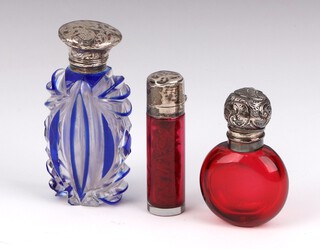 A Victorian silver mounted ruby glass scent bottle London 1890, 6cm, a circular ditto, an Edwardian circular silver ditto London 1900 7cm and a flash blue glass ditto 9cm (rubbed marks, broken lid and chipped glass) (3)