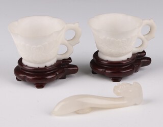 A white jade dragon belt hook, late Qing dynasty, carved with its head turned towards it tail 8cm l x 1.5cm w; together with a pair of white stone carved cups 3.5cm h x 5cm diam, on wooden stands  (5)