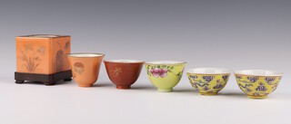 A group of five cups and a square cup holder, late Qing dynasty, comprising a pair of famille rose yellow ground cups painted with ribboned swasticas, with Guangxu marks, a famille rose yellow ground cup, painted with peony, a coral ground and gilt cup, painted with flowers and a pale coral ground cup and square cup holder painted with flowers, the largest cup - 4cm h x 6cm diameter (6)
