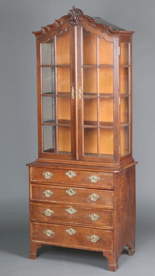 An 18th Century Dutch oak display cabinet on chest, the shaped top with shell motif and bracketed cornice, fitted shelves enclosed by astragal glazed panelled doors, the base fitted 4 drawers with embossed brass escutcheons, iron locks and replacement brass drop handles, raised on bracket feet 197cm h x 79cm w x 47cm d 