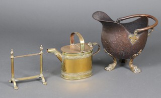 A Victorian brass hot water carrier, a brass fire dog and a copper helmet shaped coal scuttle on paw feet 