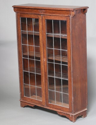 An Edwardian oak bookcase fitted adjustable shelves enclosed by lead glazed panelled doors, raised on bracket feet 122cm h x 91cm w x 26cm d 