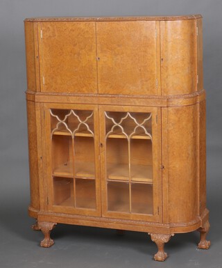 A 1950's Queen Anne style figured walnut cocktail cabinet of serpentine outline, the upper section with cocktail cabinet enclosed by panelled doors, flanked by shaped panelled doors, the base fitted shelves enclosed by astragal glazed panelled doors, raised on cabriole ball and claw supports 150cm h x 114cm w x 36cm d 
