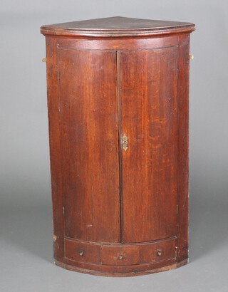 A Georgian oak bow front hanging corner cabinet fitted shelves enclosed by a panelled door, above 1 long drawer 113cm h x 66cm w x 44cm d 