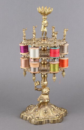 A Victorian pierced gilt brass 3 tier circular cotton reel/bobbin stand with an associated finial of a standing boy, the base supported by a seated girl with palms, raised on a Rococo style base 40cm h x 16cm diam. 