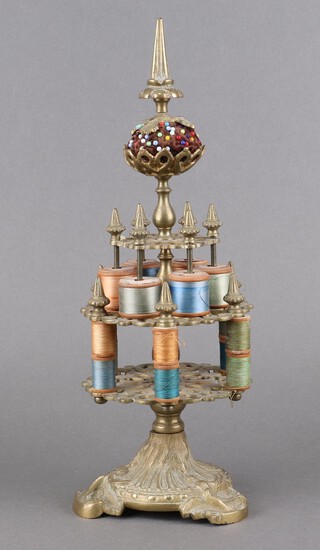 A Victorian circular pierced brass 3 tier cotton reel/bobbin stand, the finial with pin cushion, raised on a Rococo style base 36cm x 13cm 