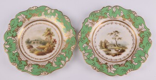A pair of 19th Century porcelain dessert plates of landscape views with figures, green and gilt rims, inscribed John Allsup, 16 St Pauls Church Yard London, 22cm 
