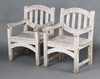 A pair of well weathered slatted wooden garden armchairs 92cm h x 60cm w x 62cm d  