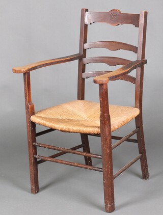 An oak open arm ladder back chair with carved peace symbol and woven rush seat