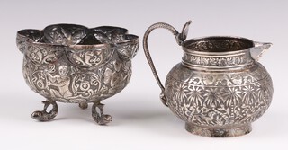 An Indian embossed white metal cream jug decorated palm trees and owls, together with a white metal sugar bowl, 168 grams 