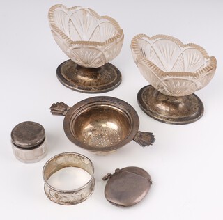 A silver engine turned vesta case Birmingham 1859, a twin handled silver tea strainer, a napkin ring, 70 grams, together with a pair of oval cut glass salts on silver bases and a small circular glass dressing table jar with silver lid (jar cracked) 