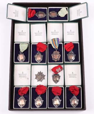 Eleven silver shield shaped sports medals with yellow gold, testing as 9ct, plaques to the centre, 112 grams including ribbons, together with a pierced silver medal  