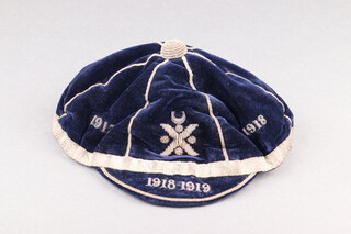 An early 20th Century Rugby / Football cap in blue cloth with gilt braiding. The crown with braided lettering "1918 1919" divided by a gilt logo of a Saltire beneath a Crescent, the brim lettered "1918-1918".  Label to interior "Aitken and Niven, 40 Queensbury St, Edinburgh"