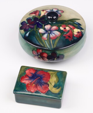 A Walter Moorcroft Spring Flowers circular lidded trinket box on a graduated blue ground, circa 1936, the bae signed, impressed marks and paper labels, 16cm diam. together with a Walter Moorcroft Hibiscus trinket box on blue/green ground, impressed marks and paper label 4cm x 9cm x 7cm  (restored)