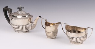 A matched silver 3 piece tea service of oval form and demi-reeded decoration, comprising teapot with ebonised handle, cream jug London 1887 and twin handled cream jug, London 1912, gross weight 520 grams  