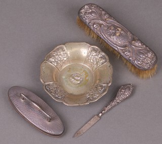 A planished silver nail buffer, an embossed silver backed hairbrush (holes), an embossed circular white metal dish and a silver handled nail file 