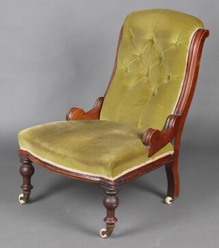 A Victorian mahogany show frame nursing chair upholstered in green buttoned material, raised on turned supports with ceramic casters 