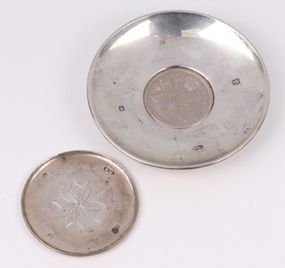 A circular silver coaster with engraved flower head London 1997 makers mark KM and a similar dish set a coin 97 grams 