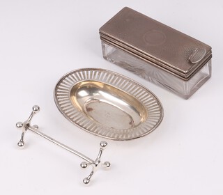 Tiffany, an oval pierced Sterling silver dish 8cm x 6cm, the base marked Tiffany & Co 17020 5706 Sterling Silver (some salt? corrosion marks to the centre), a silver knife rest 50 grams, together with a rectangular glass and and silver mounted dressing table jar with hinged lid (glass a/f) 