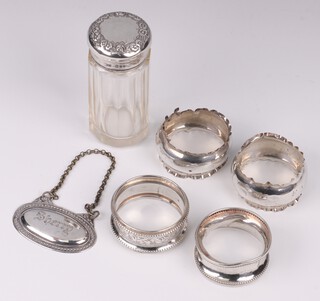 Four silver napkin rings (misshapen and dented) and a faceted glass pin jar with embossed silver lid, 9cm, together with a Sherry decanter label 
