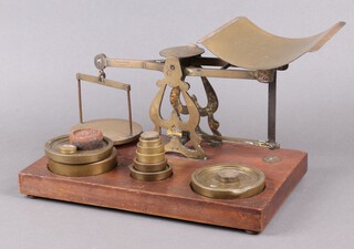 S Morden & Co. London, a pair of brass postage scales, raised on an oak base together with 12 associated brass weights - 2 x 4lbs (1 damaged to the edge), 2lb, 1lb, 8 ozs, 6 ozs, 4 ozs, 2 ozs x 2, 1 oz x 2, together with an iron 8 oz weight 