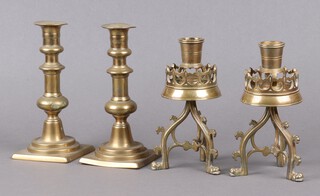 A pair of Victorian Gothic style pierced brass candlesticks on shaped supports 15cm x 7cm (slightly misshapen) together with a pair of 18th Century brass candlesticks with ejectors on square bases 18cm, bases marked M4 (both with misshapen sconces, 1 is loose and requires soldering) 