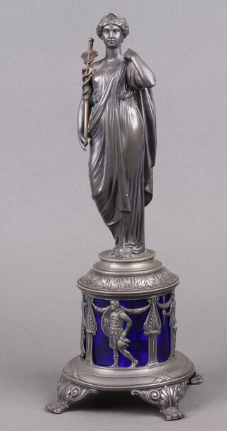A WMF figure depicting The Goddess of Medicine, raised on a pierced cylindrical base with blue glass liner decorated figures of warriors, the base marked MB, 34cm h 