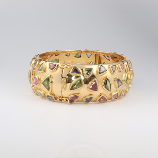A lady's impressive yellow gold marked 18K hinged bangle, set 66 multi coloured sapphires approx 100ct in total, 8cm diameter, 112.8 grams gross