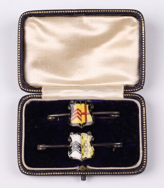 Two unmarked silver and enamelled bar brooches decorated armorial shields in a plush case 
