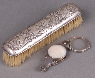 An embossed silver clothes brush decorated Botticelli angels together with a magnifying glass
