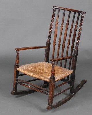 A 1930's beech framed stick and rail back rocking chair with spiral turned decoration and woven rush seat 