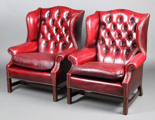 A pair of wing armchairs upholstered in red buttoned leather, raised on square tapered supports 109cm h x 77cm w x 66cm d 