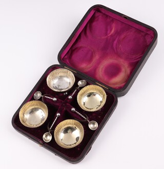 A set of 4 circular silver salts with parcel gilt interiors and demi-reeded decoration, raised on bun feet, London 1884, by Martin Hall and Company, together with 4 silver salt spoons London 1884, 83 grams, cased  