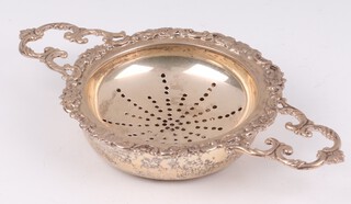 A circular silver twin handled tea strainer and stand, London 1962 by William Cummings & Sons Ltd. 133 grams 
