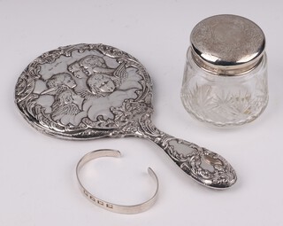 An Edwardian silver backed hand mirror decorated Botticelli angels Birmingham 1904, a cut glass dressing table jar with silver lid Chester 1922, marks rubbed and a Solvar silver bangle
