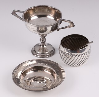A circular embossed silver salt London 1887 together with a salt spoon and a twin handled silver trophy cup (marks rubbed), a circular silver Armada dish London 1958, 137 grams 
