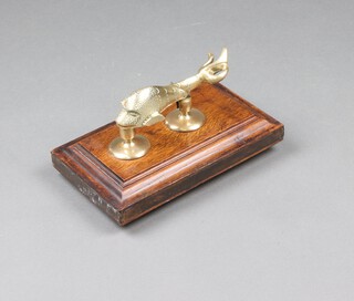 A brass door knocker in the form of a dolphin on a rectangular oak stand 18cm h x 31cm w x 19cm d 