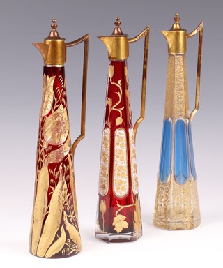 An Art Nouveau Bohemian aquamarine and gilt octagonal overlay and etched glass ewer with gilt mounts (slight chip to base, hinge a/f), together with a similar red glass ewer with vinous decoration (slight chip to base) and 1 other deeply etched flowers (chips to base) each 30cm high 